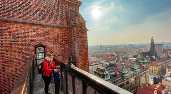 Kobieta z dzieckiem na moście pokutnic we Wrocławiu podziwia panoramę miasta.