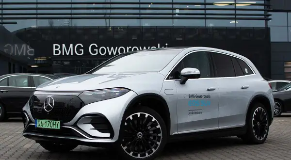 Srebrny Mercedes EQS SUV z napisem "BMG Goworowski EQS SUV jazda testowa" przed salonem samochodowym.