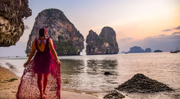 Kobieta w zwiewnej sukni spaceruje po plaży w Ao Nang, podziwiając skaliste wysepki o zachodzie słońca.