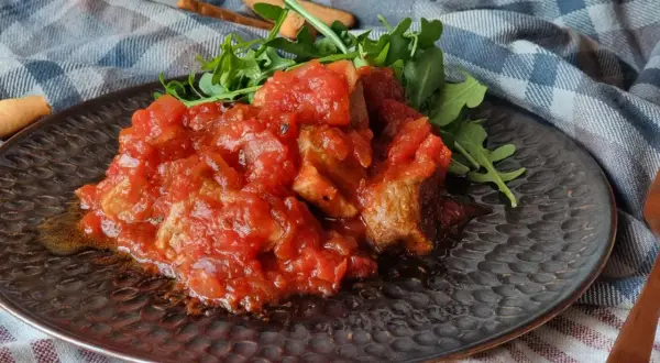 Magro con tomate, un plato casero con trozos de carne tierna bañados en una salsa de tomate casera, acompañado de rúcula fresca.