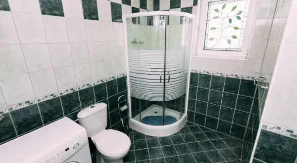 Łazienka z pralką, toaletą i narożną kabiną prysznicową. Widać syfon pod prysznic, który zapewnia prawidłowe odprowadzanie wody.