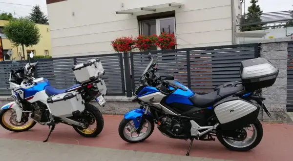 Dwa motocykle turystyczne z kuframi stoją przed nowoczesnym domem z kwiatami na balkonie.