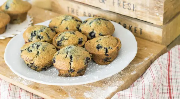 Plate of delicious muffin myrtille, sprinkled with powdered sugar, on a wooden board.