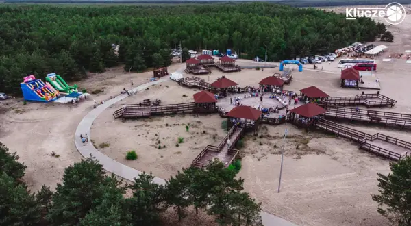 Drewniane zadaszone altany i ścieżki na piaszczystym terenie w miejscowości Klucze, otoczone lasem.