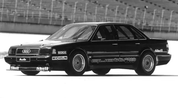 Czarny Audi 5000 Quattro na torze wyścigowym, z logotypami Boge, Michelin i Shell.