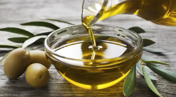 Olio evo l'extravergine, dorato e puro, viene versato in una ciotola di vetro. Olive e foglie di ulivo completano la scena.