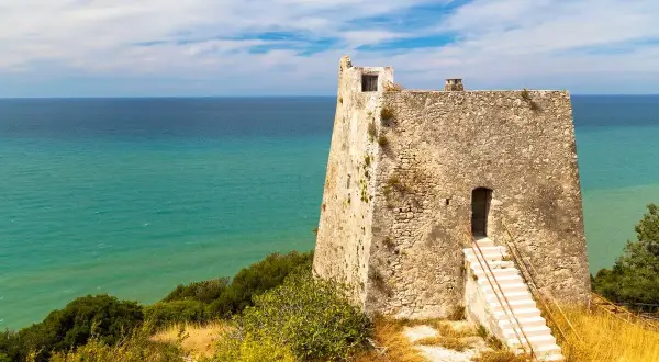 Torre costiera in pietra con mare turchese sullo sfondo, un luogo suggestivo tra i tanti posti da visitare in Puglia.