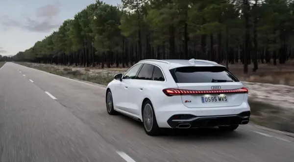 Białe Audi A5 Avant 2025 pędzi pustą drogą wśród sosnowego lasu.