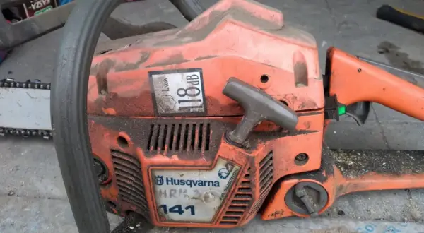 Pomarańczowa piła łańcuchowa Husqvarna 141, z widocznymi danymi technicznymi, gotowa do pracy.