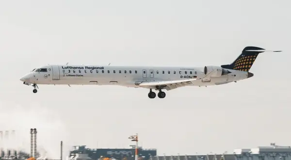 Samolot Lufthansa Regional z podwoziem wysuniętym do lądowania, leci nisko nad lotniskiem.
