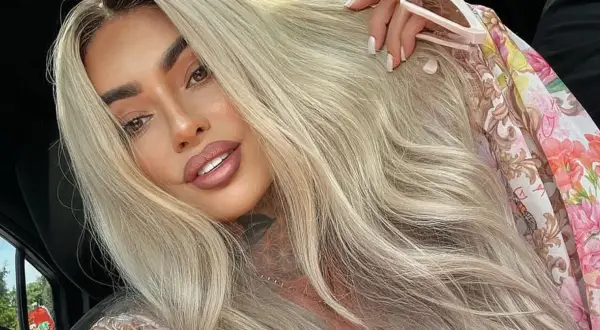 Ania Królowe Życia z blond włosami i tatuażem na szyi, w kwiecistej bluzce.