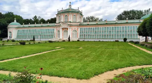 Przepiękny, różowo-zielony pałac z przeszklonymi ścianami, przypominający **ogród zimowy w domu**, otoczony jest zadbanym trawnikiem i alejkami.