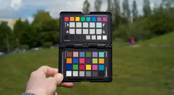 Dłoń trzyma otwartą kartę X-Rite ColorChecker, aby ustawić prawidłową temperaturę barwową w plenerze.