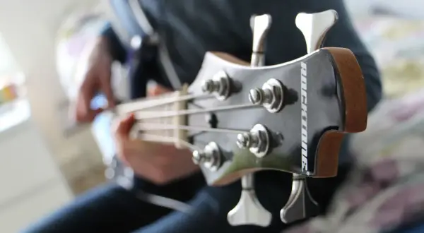 Osoba gra na gitarze basowej, wydobywając głębokie dźwięki na basie.
