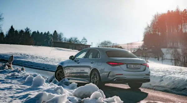 Srebrny Mercedes C 300 na tle ośnieżonych wzgórz i lasu. Zima nie straszna temu eleganckiemu autu.