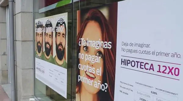 Anuncios de hipotecas en un escaparate. Uno muestra tres hombres y pregunta "¿Te imaginas no pagar cuotas el primer año?". Otro, con una mujer, dice "Deja de imaginar. No pagues cuotas el primer año. HIPOTECA 12X0". Se ve un **euribor forecast** en la ...