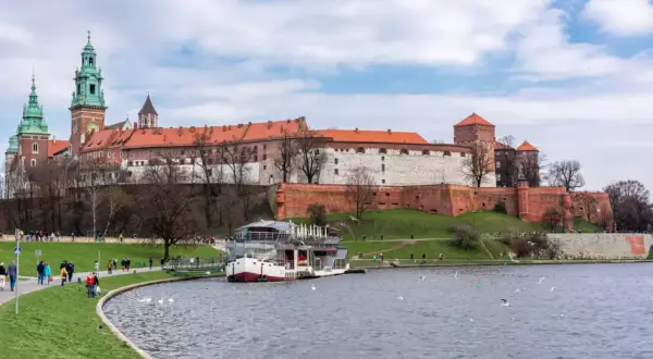 Zamek Królewski na Wawelu nad Wisłą, z łodzią i spacerującymi ludźmi.