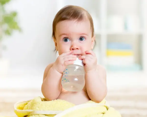 Ein süßes Baby mit blauen Augen hält eine Flasche und trinkt. Es scheint, als ob dieses Baby zu viel trinkt, aber es genießt jeden Schluck.