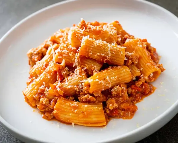 Un piatto invitante di pasta alla zozzona, con rigatoni conditi con un ricco ragù e abbondante parmigiano grattugiato.