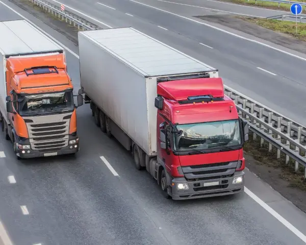 Dwa ciężkie tiry na autostradzie. Czerwony i pomarańczowy, każdy z dużą naczepą. Maksymalny nacisk na oś naczepy to klucz do bezpiecznego transportu.