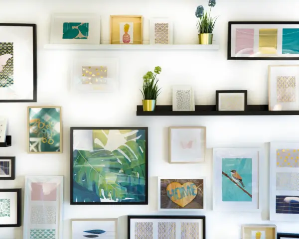 Mur décoré de cadres aux motifs variés : papillons, ananas, feuilles tropicales, oiseaux. Une collection d'art inspirante, parmi les meilleurs sites d'artistes.