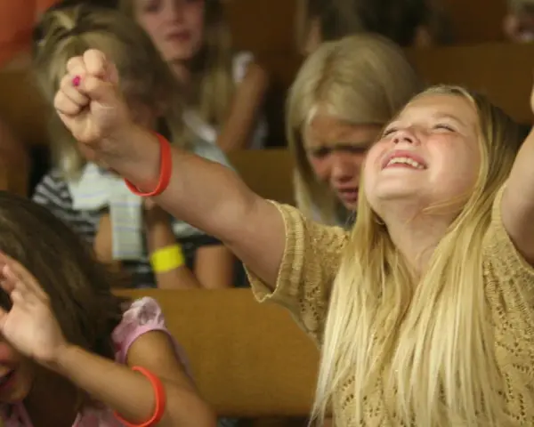 Junge Mädchen erleben emotionale Momente bei einer evangelistischen Religionsveranstaltung, eine jubelt, die andere weint.
