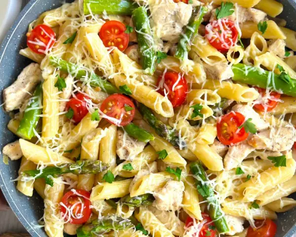 Penne z kurczakiem, szparagami i pomidorkami koktajlowymi, posypane parmezanem. Pyszne danie, które zachwyci każdego smakosza.