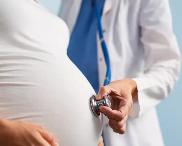 Lekarz osłuchuje brzuch ciężarnej kobiety stetoskopem. Dbałość o zdrowie w ciąży to podstawa.
