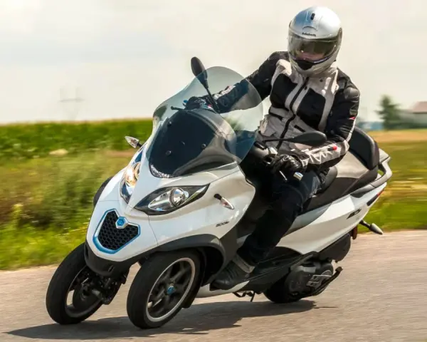 Biały Piaggio MP3 500 z kierowcą w kasku pędzi po drodze. Zastanawiasz się nad jego spalaniem?