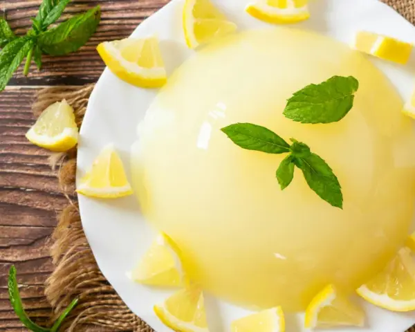 Delizioso gelo di limone su piatto bianco, decorato con spicchi di limone fresco e foglie di menta.