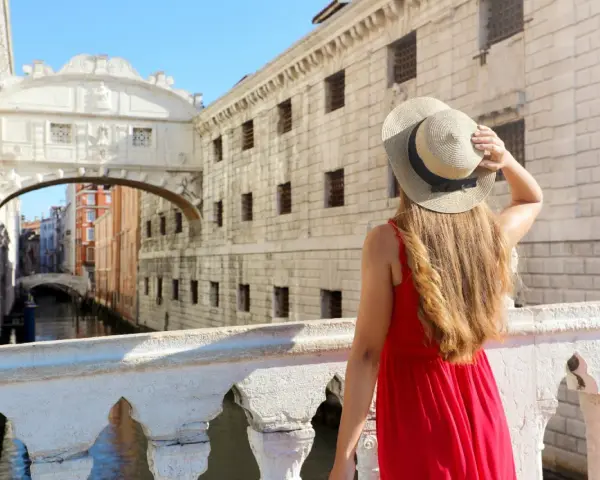 Una donna con un cappello di paglia ammira il Ponte dei Sospiri, un iconico ponte degli innamorati a Venezia, con i suoi canali e palazzi storici.