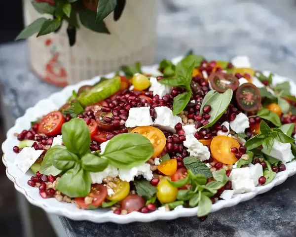 En färgglad sallad med granatäpple, tomater, fetaost och basilika, perfekt som sallad till grillat.