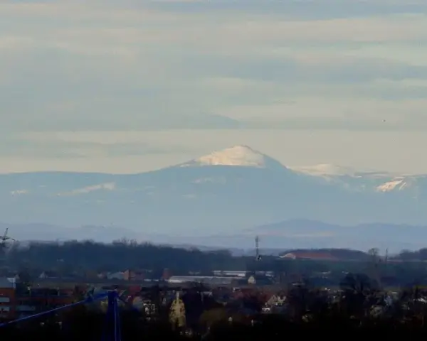 Widok na Śnieżkę i Karkonosze z Wrocławia. Widać ośnieżone szczyty górskie na tle błękitnego nieba.