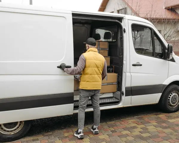 Kurier otwiera drzwi białego busa dostawczego, w którym widać paczki. Zastanawiasz się, ile waży bus dostawczy?