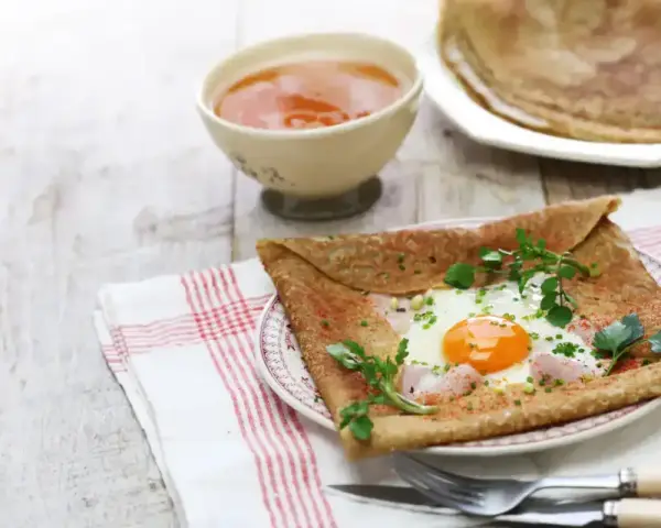 Crêpe de sarrasin garnie d'un œuf au plat, de jambon et d'herbes fraîches, servie avec une compote.