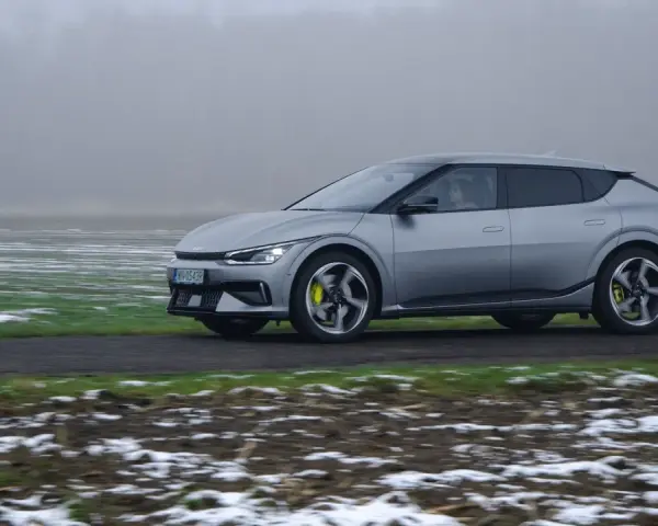 Srebrna Kia EV6 jedzie po drodze, otoczona polami z resztkami śniegu.