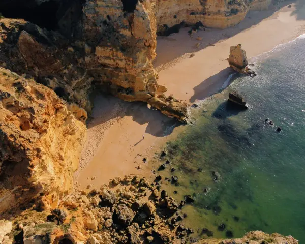 Malownicze klify i piaszczysta plaża w Portugalii. Morze o turkusowym odcieniu obmywa skaliste wybrzeże, tworząc idealne miejsce na spacer.