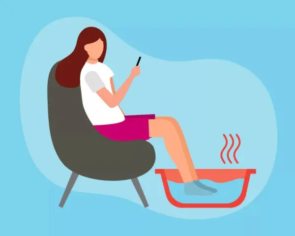 A woman relaxes in a chair, enjoying a soothing foot soak while scrolling on her phone.