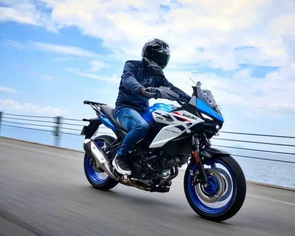 Motocyklista na niebiesko-białym Suzuki SV650X, idealnym motocyklu do 35kW, jedzie wzdłuż wybrzeża.