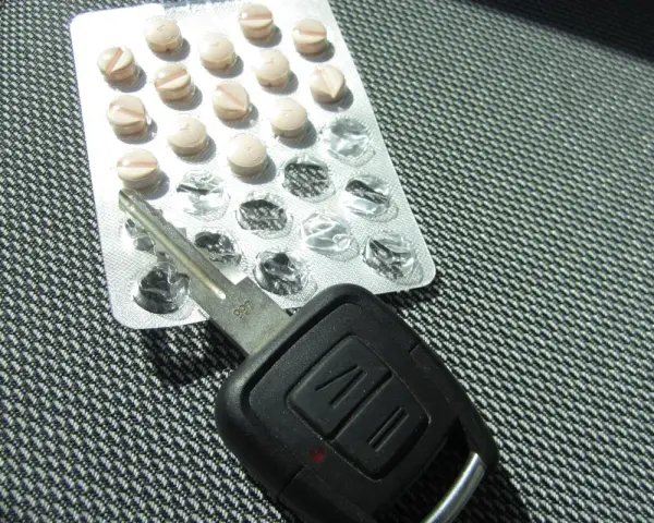 Tabletten und Autoschlüssel liegen nebeneinander. Tilidin autofahren ist gefährlich und illegal.