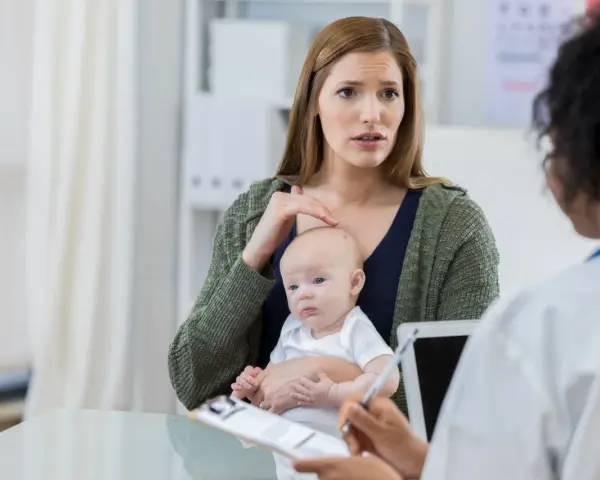 Zaniepokojona mama z niemowlęciem na rękach rozmawia z lekarzem. Zastanawia się nad chwilowym zawieszaniem się dziecka.