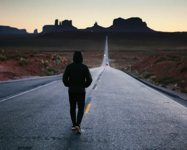 Człowiek idzie pustą drogą w Monument Valley, pogrążony w mysleniu tunelowym, z widokiem na skalne formacje w oddali.