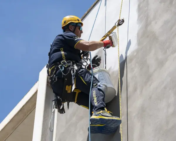 Trabajador en altura realiza instalación SATE, aplicando revestimiento en fachada con equipo de seguridad.