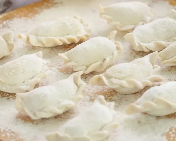 Surowe pierogi, gotowe do gotowania, posypane mąką. Wyglądają jak najlepsze ciasto na pierogi, które mama kiedyś robiła.