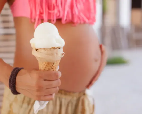 Schwanger und Lust auf Eis? Eine Frau hält ein Eis in der Hand, während sie ihren Bauch streichelt.