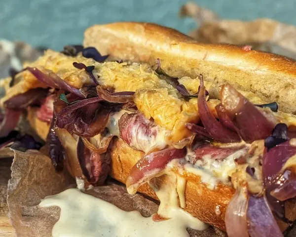 Ein saftiger Philly Cheesesteak-Sandwich mit geschmolzenem Käse, karamellisierten roten Zwiebeln und zartem Rindfleisch auf einem Baguette.