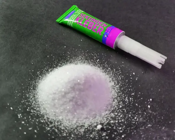 A pile of white granular material sits next to a tube of "Sekunden Kleber" super glue, ready for a quick fix.