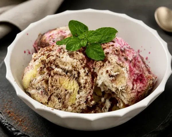 Schüssel mit Zuppa Inglese Gelato, garniert mit Minze und Schokoladenraspeln. Ein Löffel liegt daneben.