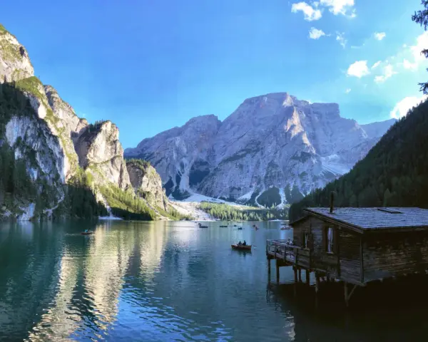 Malownicze jezioro w Dolomitach, z górami w tle i drewnianym domkiem na wodzie. Idealne miejsce na camping i podziwianie natury.