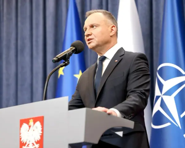 Prezydent Andrzej Duda przemawia przy mównicy z godłem Polski. Za nim flagi UE i NATO. Może to być związane z ułaskawieniem prezydenta.